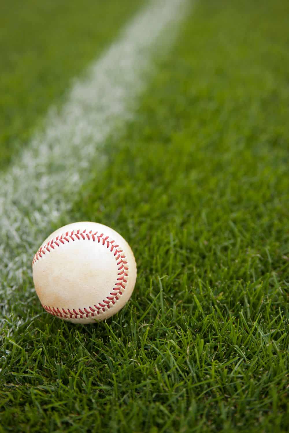 A baseball rests on lush sports turf, its white surface contrasting against the vibrant green grass near a crisp chalk line on the field.